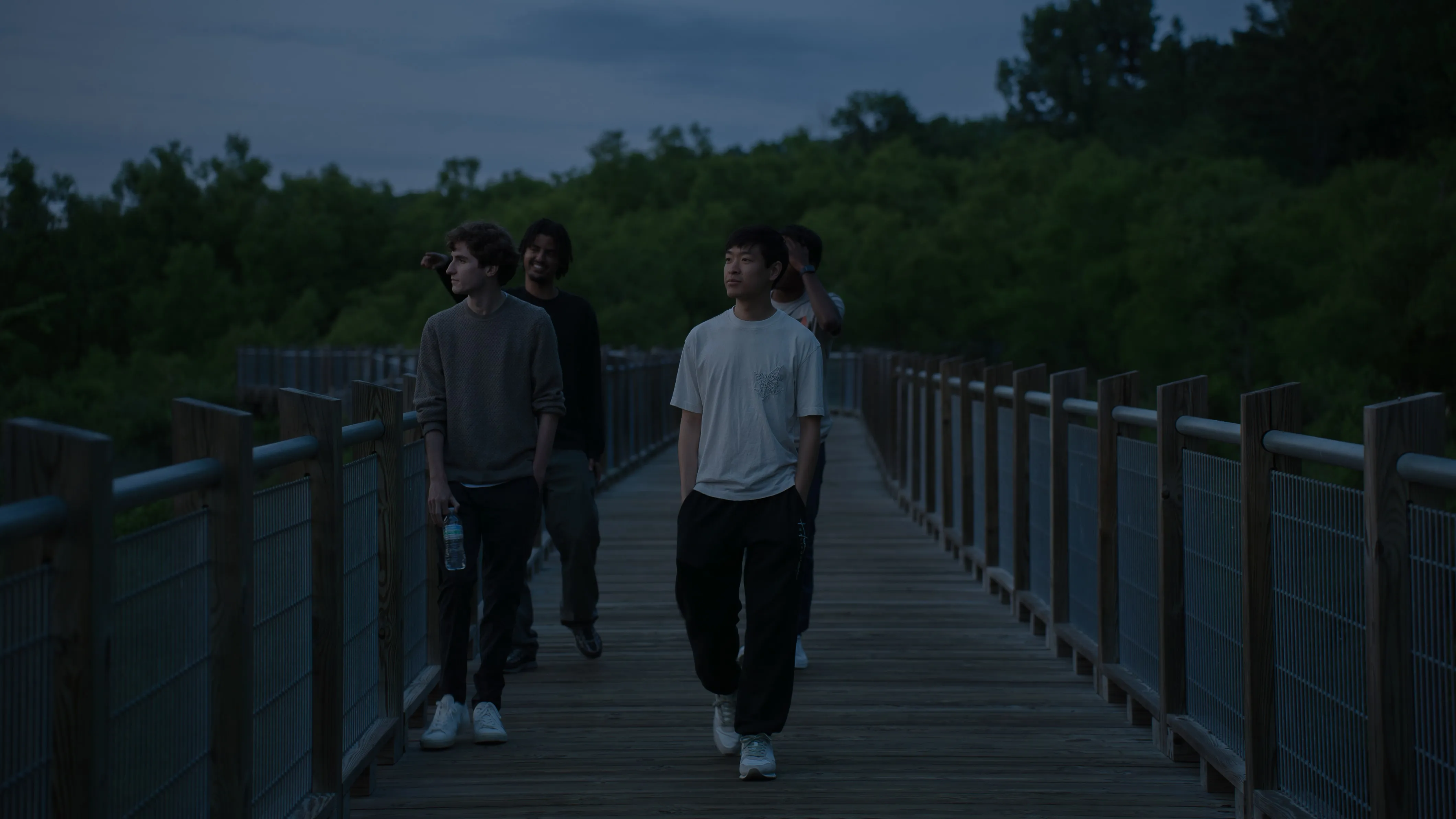 Guys walking down boardwalk over swamp at night